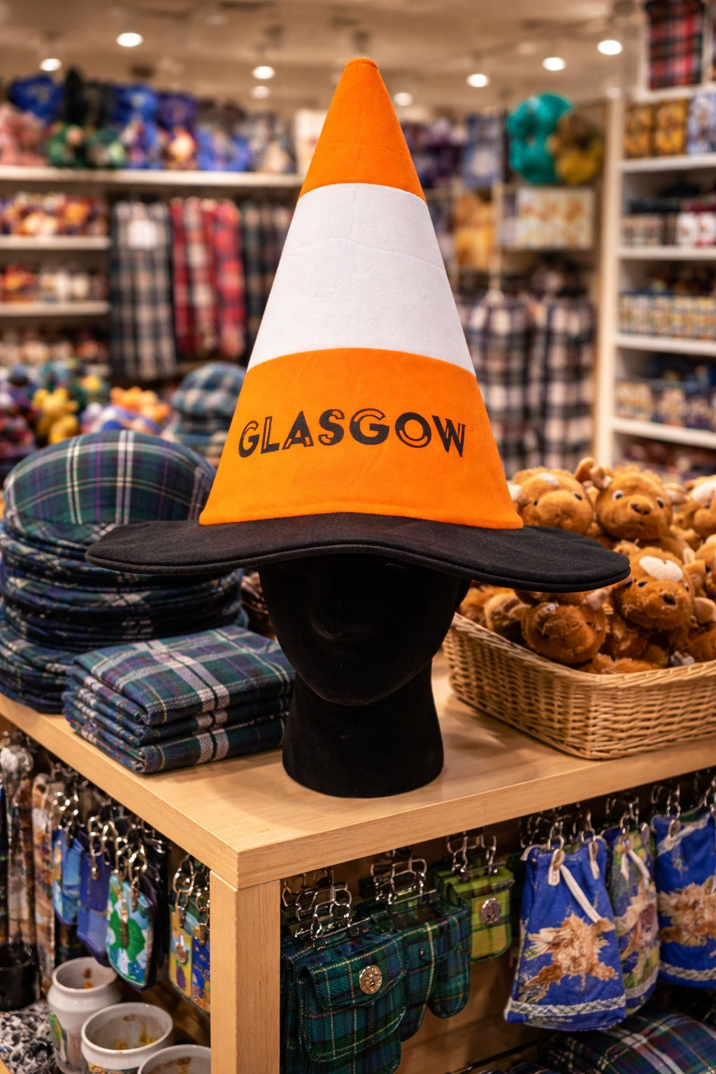 Cone-shaped hat with 'Glasgow' text on a mannequin head in a store setting.