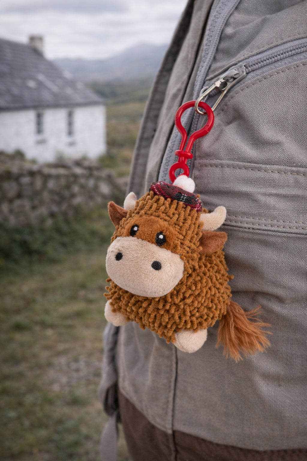 Plush Highland cow keychain attached to a bag on a scenic background.