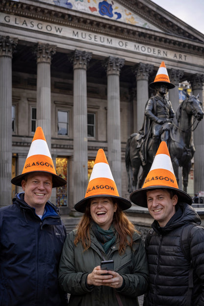 Three people wearing novelty Glasgow cone hats with 'Glasgow' on them in front of the Duke of Wellington Statue at Glasgow's Museum of Modern Art.