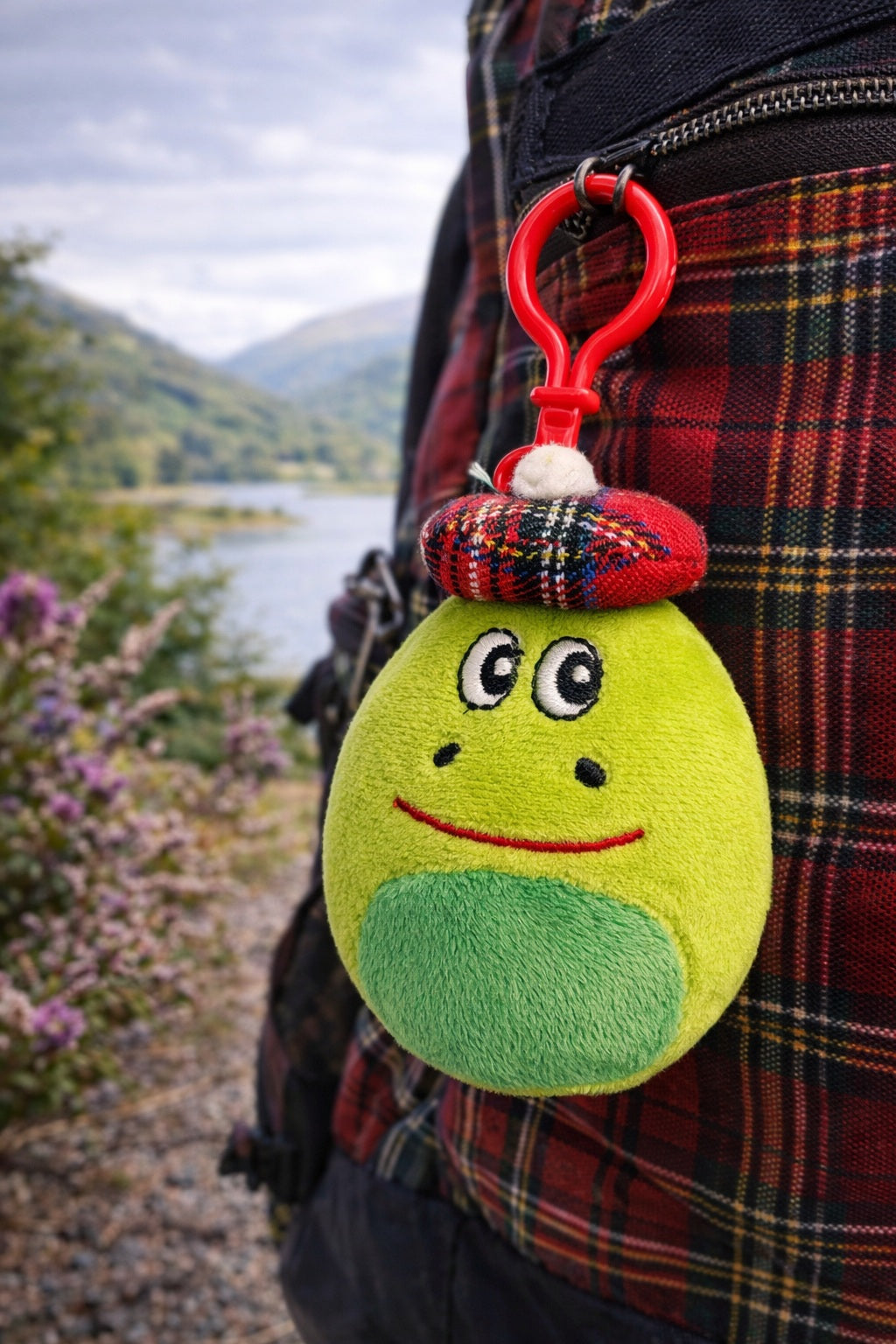 Green plush nessie keychain attached to a tartan bag with a scenic background.