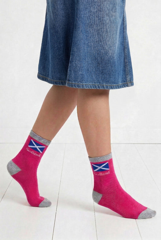 Person wearing pink socks with Scottish flag design and a denim skirt on a white floor.