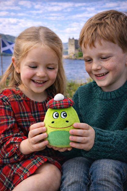 Two children holding a green plush Nessie soft toy with a castle in the background.