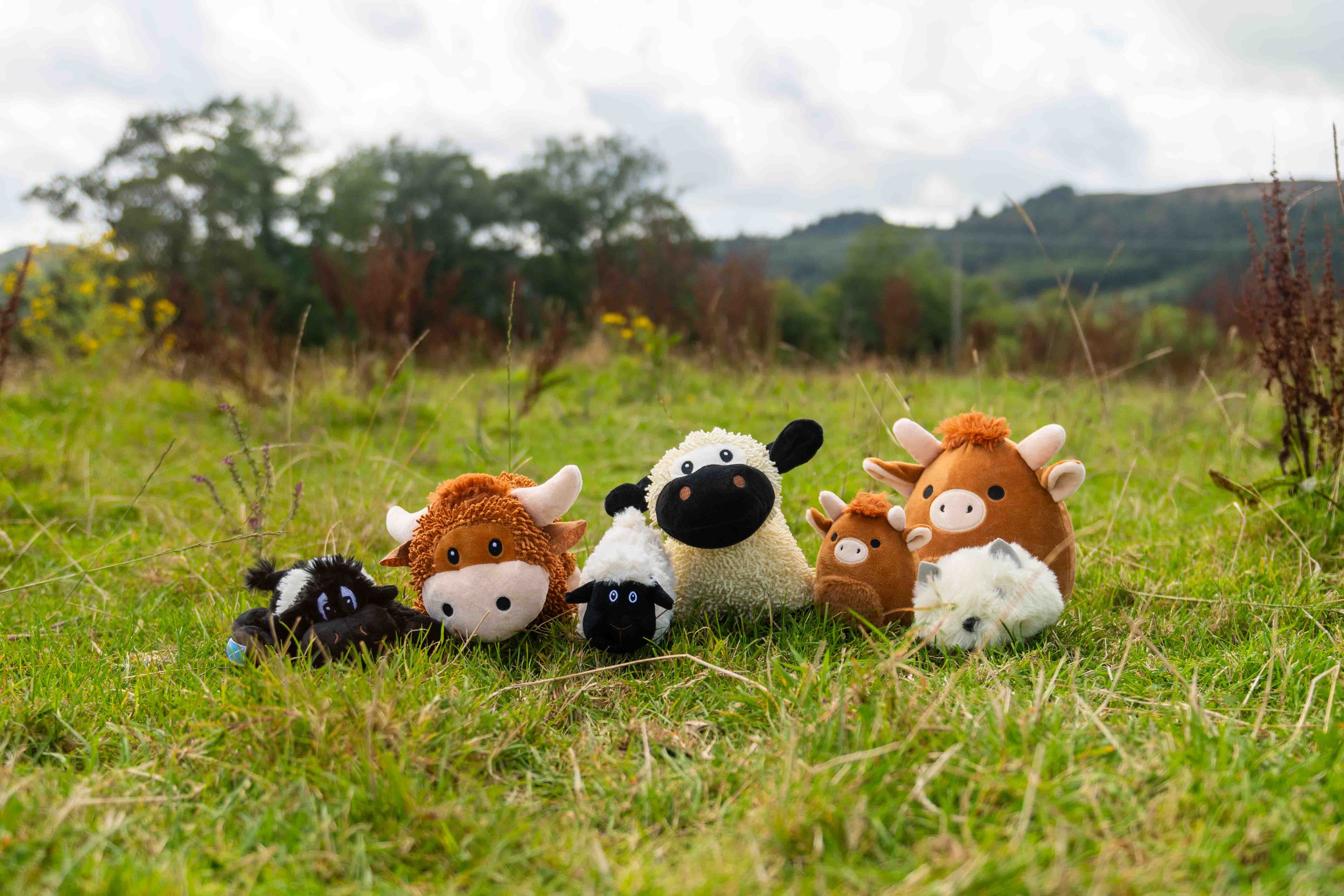 Plush toys resembling farm animals on a grassy field with a natural background