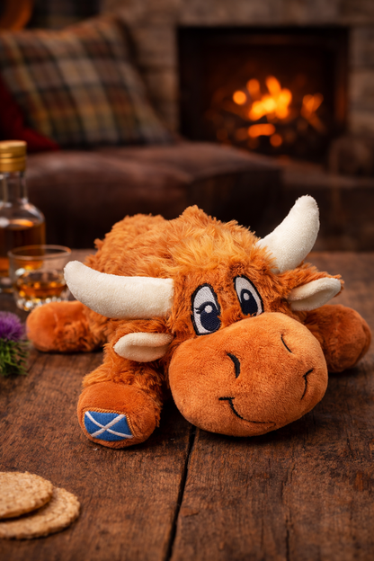 Plush Highland cow soft toy on a wooden surface with a fireplace in the background.